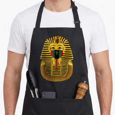 Tablier de cuisine noir avec le masque doré de Toutankhamon orné d'une coiffe striée noire et jaune et d'un symbole ankh coloré sur le visage.