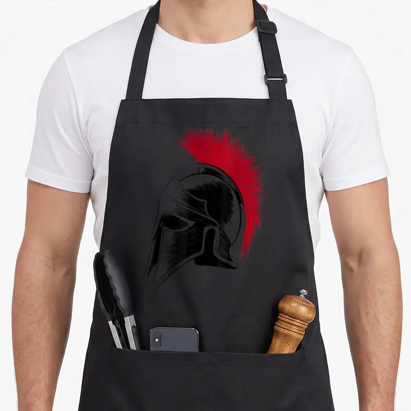Tablier de cuisine noir avec illustration d'un casque spartiate noir et crinière rouge vif de style gravure.