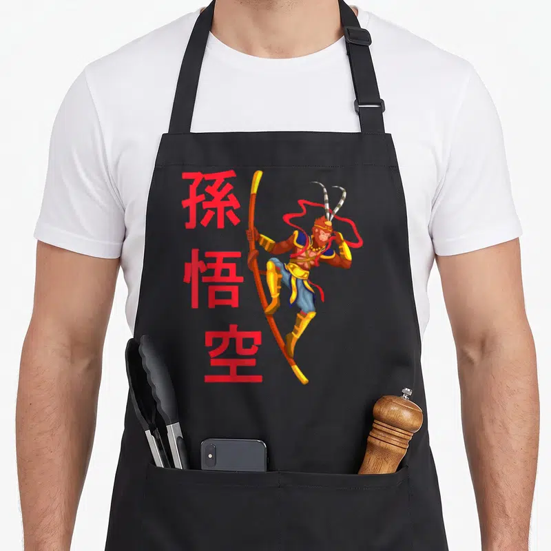 Tablier de cuisine noir avec illustration colorée de Sun Wukong tenant une baguette et des symboles chinois rouges.