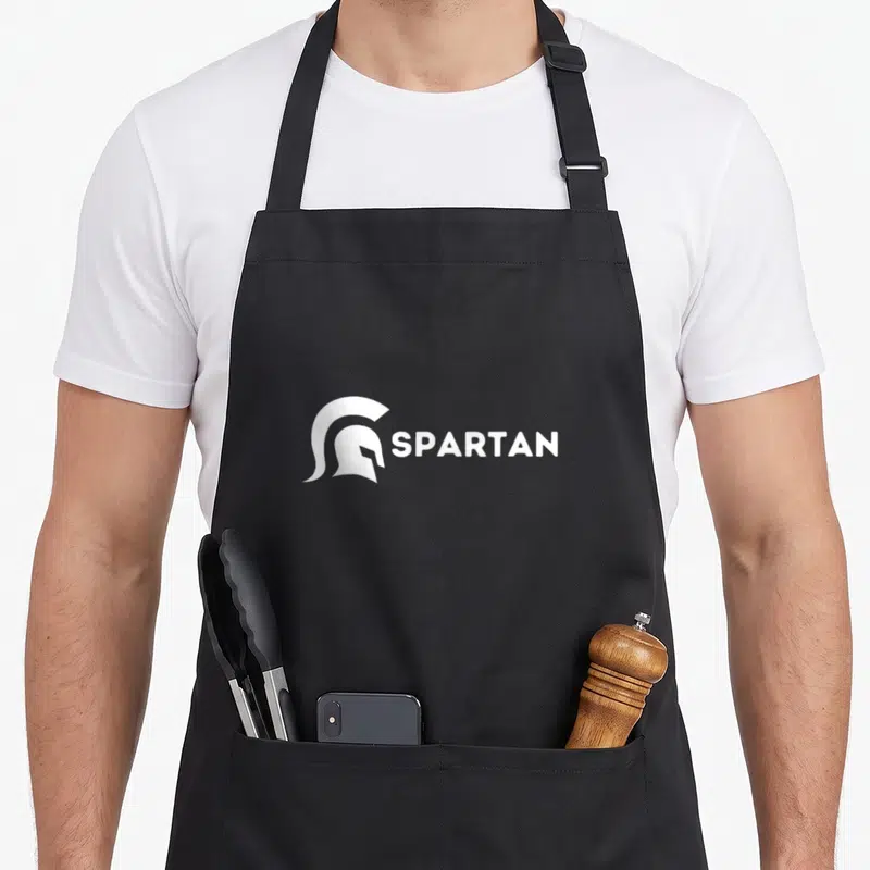 Tablier de cuisine noir avec illustration blanche de casque de gladiateur et texte SPARTAN.