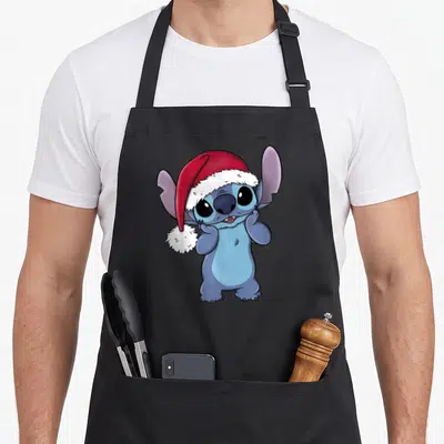 Tablier de cuisine noir avec Stitch portant un chapeau de Noël rouge et blanc, les mains sur les côtés du visage.