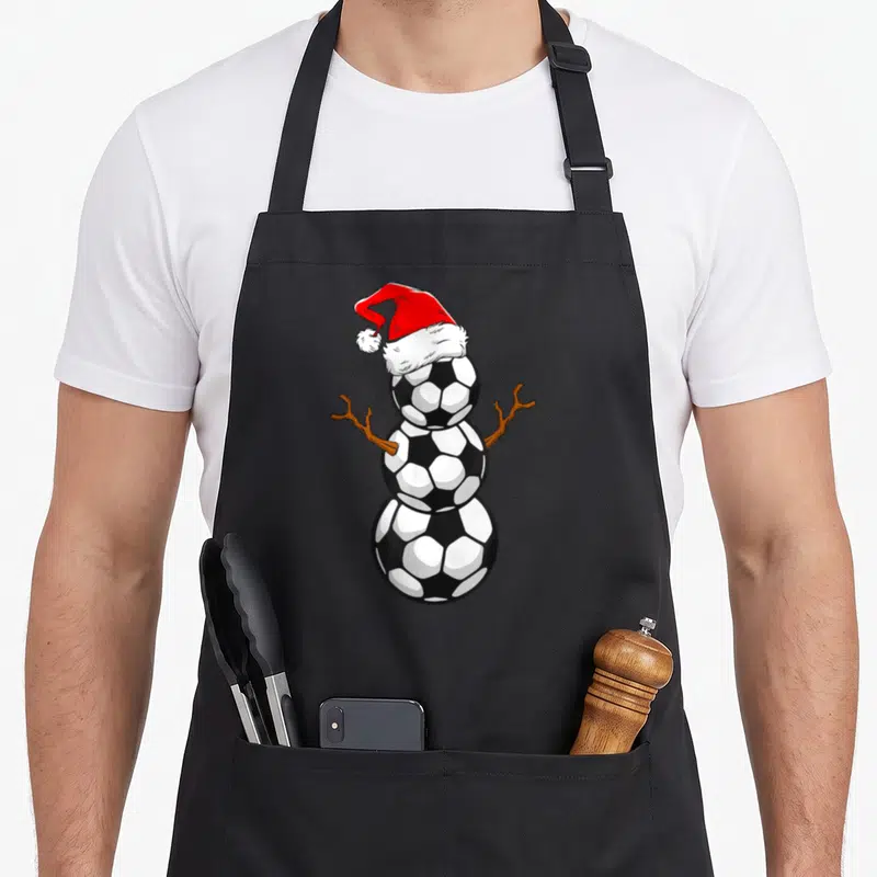 Tablier de cuisine noir avec un bonhomme de neige joueur de football portant un chapeau de Père Noël rouge.