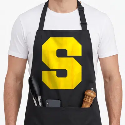 Tablier de cuisine noir avec une grande lettre S jaune vif au centre du torse.