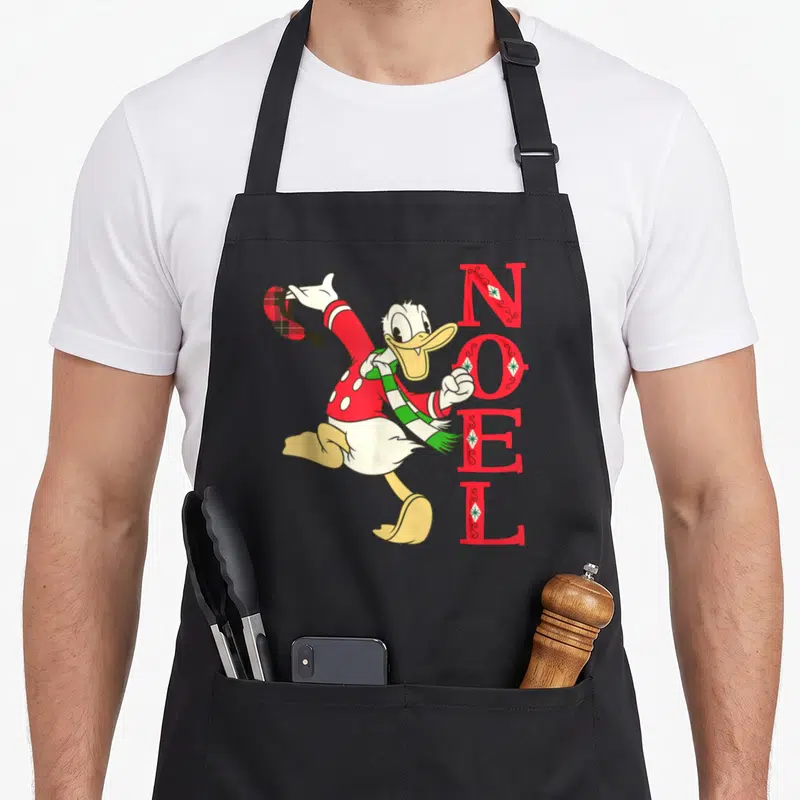 Tablier de cuisine noir avec Donald Duck en pull rouge et scarpe verte à côté du texte NOEL en lettres rouges décorées.