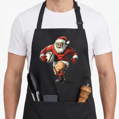 Tablier de cuisine noir avec illustration d'un Père Noël joueur de rugby portant un maillot rouge et tenant un ballon.