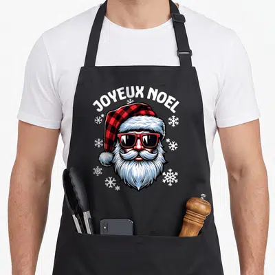 Tablier de cuisine noir avec illustration colorée d'un Père Noël portant des lunettes de soleil et un bonnet à carreaux rouge et noir.