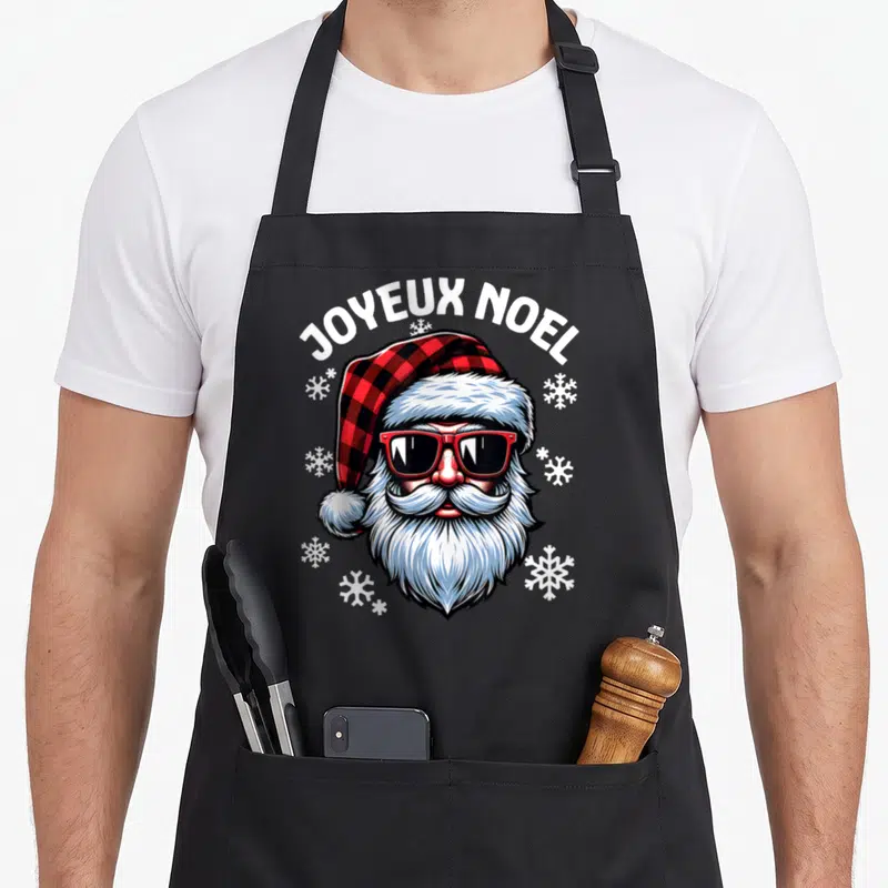 Tablier de cuisine noir avec illustration colorée d'un Père Noël portant des lunettes de soleil et un bonnet à carreaux rouge et noir.