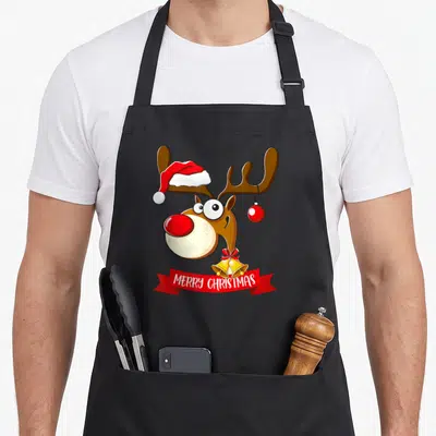 Tablier de cuisine noir avec illustration colorée d'un renne festif portant un bonnet rouge et des cloches dorées.