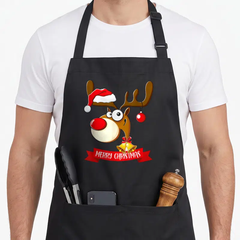 Tablier de cuisine noir avec illustration colorée d'un renne festif portant un bonnet rouge et des cloches dorées.