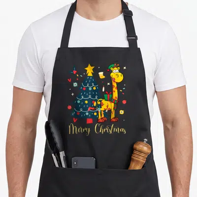 Tablier de cuisine noir avec sapin de Noël, girafe souriante en bonnet et texte Merry Christmas en lettres dorées scintillantes.