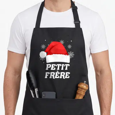 Tablier de cuisine noir avec chapeau Père Noël rouge et l'inscription Petit Frère en lettres blanches entourée de motifs de neige.