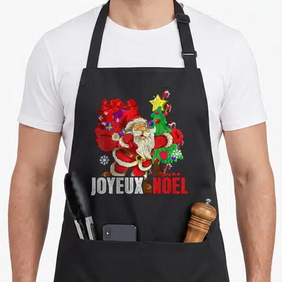 Tablier de cuisine noir avec Père Noël rouge, sac de cadeaux, sapin décoré et texte JOYEUX NOËL en bas.