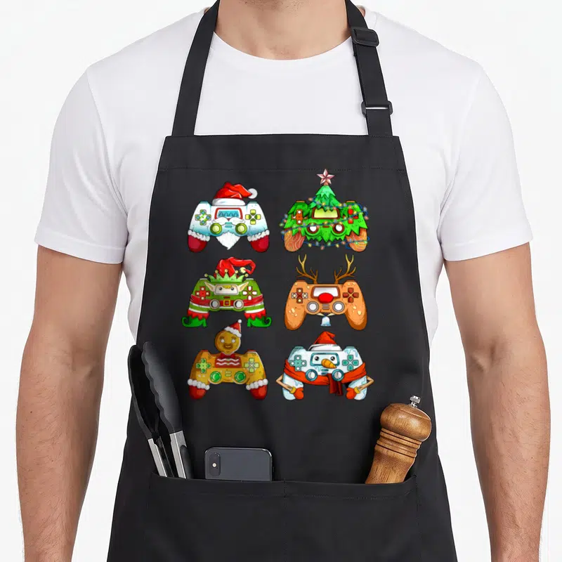 Tablier de cuisine noir avec six manettes de jeu vidéo déguisées en personnages de Noël comme un Père Noël ou un elfe.