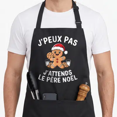 Tablier de cuisine noir avec un pain d'épice souriant en chapeau rouge et blanc tenant des biscuits.