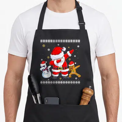 Tablier de cuisine noir avec un Père Noël faisant le dab entouré d'un bonhomme de neige et d'un biscuit de Noël.