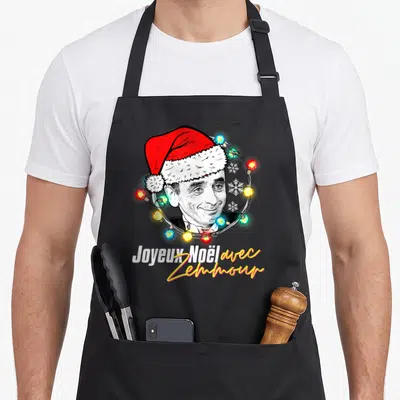 Tablier de cuisine noir avec portrait de Zemmour en bonnet de Père Noël et guirlande colorée.