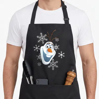 Tablier de cuisine noir avec le visage souriant d'Olaf et des flocons blancs dispersés autour.