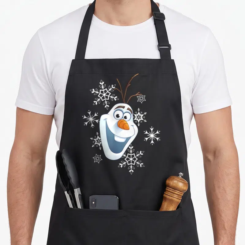 Tablier de cuisine noir avec le visage souriant d'Olaf et des flocons blancs dispersés autour.