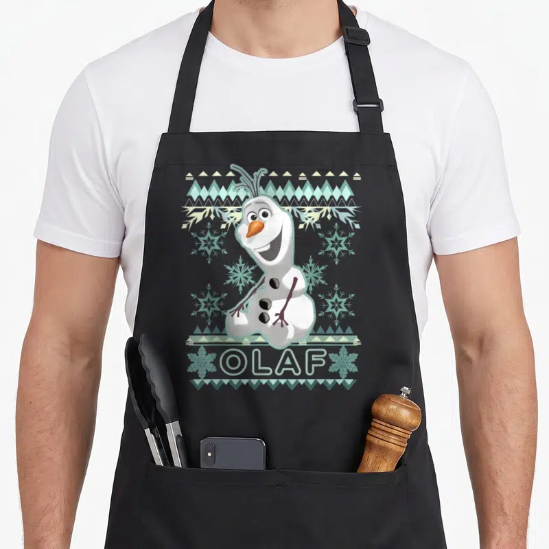 Tablier de cuisine noir avec Olaf souriant entouré de motifs de neige et de bleu clair sur fond gris uni.