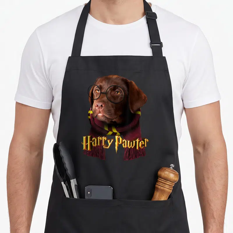 Tablier de cuisine noir avec un chiot labrador portant des lunettes rondes et une écharpe à franges rouges et jaunes.