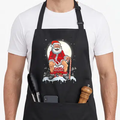 Tablier de cuisine noir avec illustration colorée d'un Père Noël souriant assis sur une cheminée enneigée.