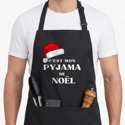 Tablier de cuisine noir avec une casquette de Père Noël et le texte C'est mon pyjama de Noël en blanc.