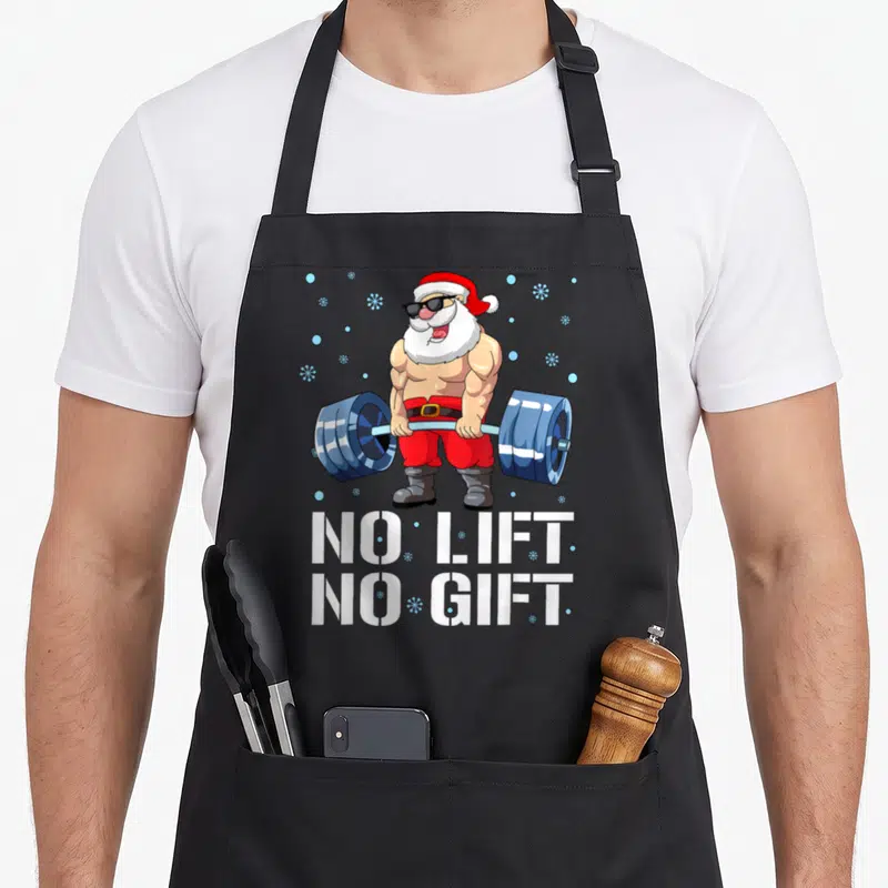 Tablier de cuisine noir avec illustration d'un Père Noël musclé tenant une barre de poids bleue et le texte blanc « No Lift No Cadeau ».