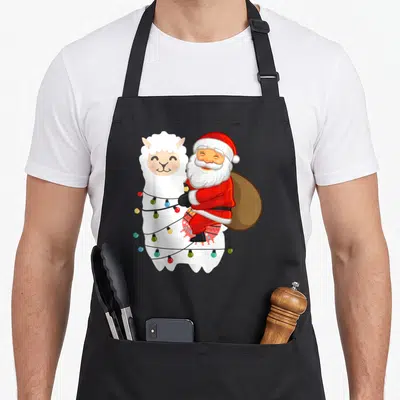 Tablier de cuisine noir avec illustration d'un Père Noël en pyjama accroché à un lama orné de lumières de Noël.