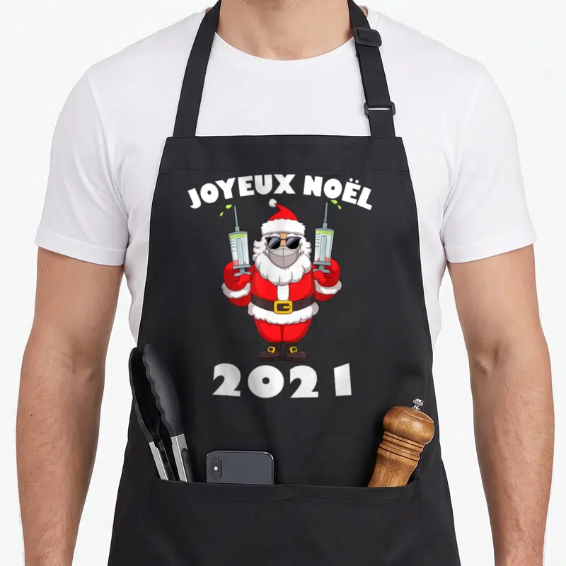 Tablier de cuisine noir avec un Père Noël en masque, lunettes de soleil et deux seringues vertes.