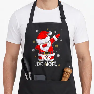 Tablier de cuisine noir avec un Père Noël en train de faire le dab entouré de flocons dorés et blancs.