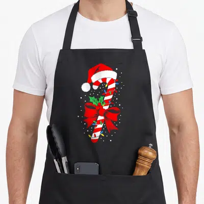 Tablier de cuisine noir avec illustration colorée d'une canne à sucre de Noël coiffée d'un bonnet rouge et blanche.