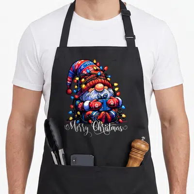 Tablier de cuisine noir avec un gnome de Noël entouré de lumières et le texte Merry Christmas en bas.