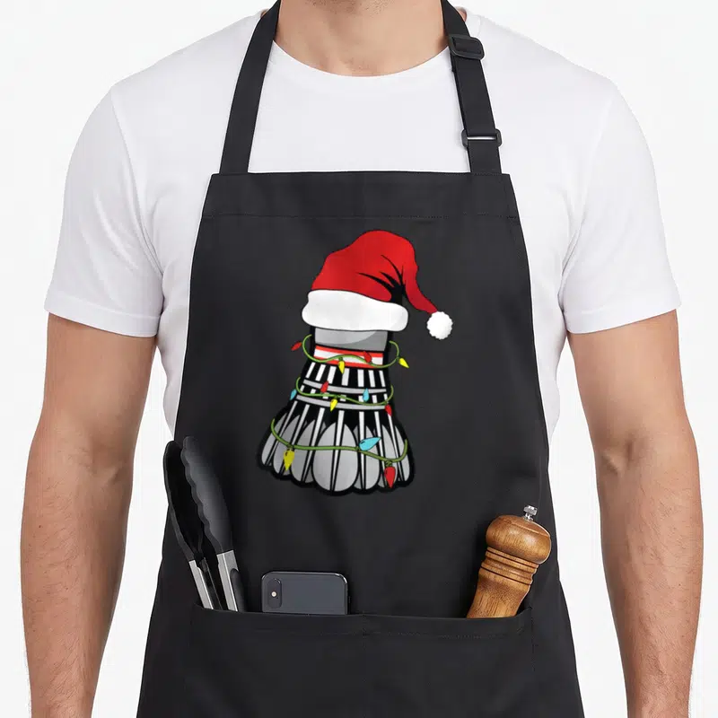 Tablier de cuisine noir avec un shuttle de badminton portant un bonnet de Père Noël et des lumières de Noël.