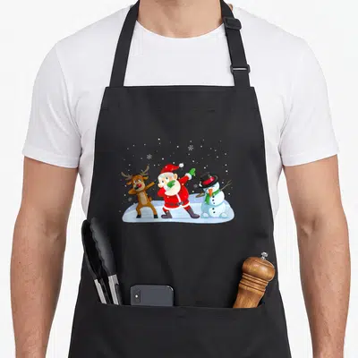 Tablier de cuisine noir avec Père Noël, renne et bonhomme de neige en train de faire le dab dans la neige.