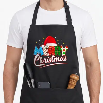 Tablier de cuisine noir avec inscription Merry Christmas en carreaux colorés et bonnet de Père Noël rouge sur fond uni.