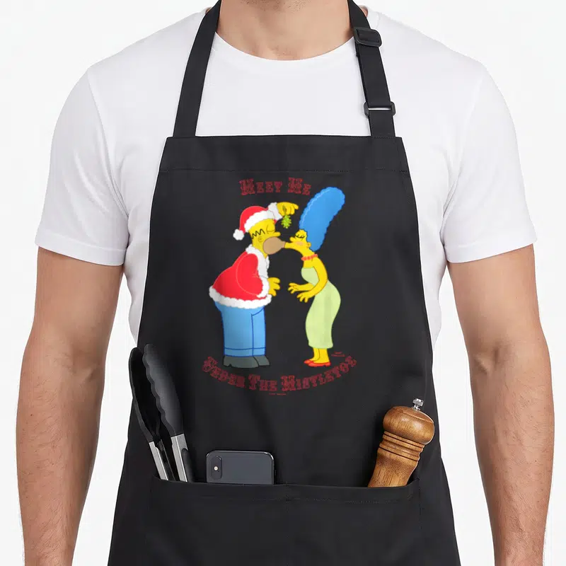 Tablier de cuisine noir avec Homer et Marge sous le gui et l'inscription Meet Me Under the Mistletoe en rouge.