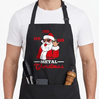 Tablier de cuisine noir avec un Père Noël rock aux lunettes de soleil et le texte Metal Christmas imprimé en rouge et blanc.