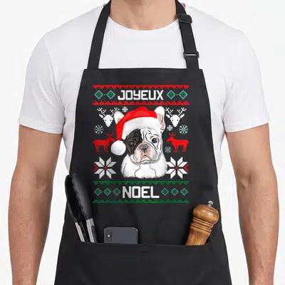 Tablier de cuisine noir avec illustration d'un bouledogue français portant un bonnet de Père Noël sur fond de motifs festifs rouges et verts.