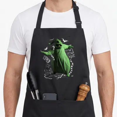 Tablier de cuisine noir avec un personnage vert en tricot, des dés et le texte I'm the Oogie Boogie Man en blanc.