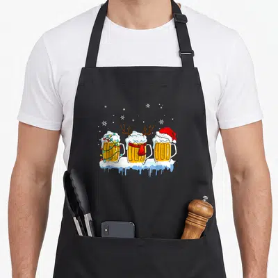 Tablier de cuisine noir avec trois mug de bière décorés de guirlandes, de bois de renne et d'une casquette de Père Noël sur la neige.