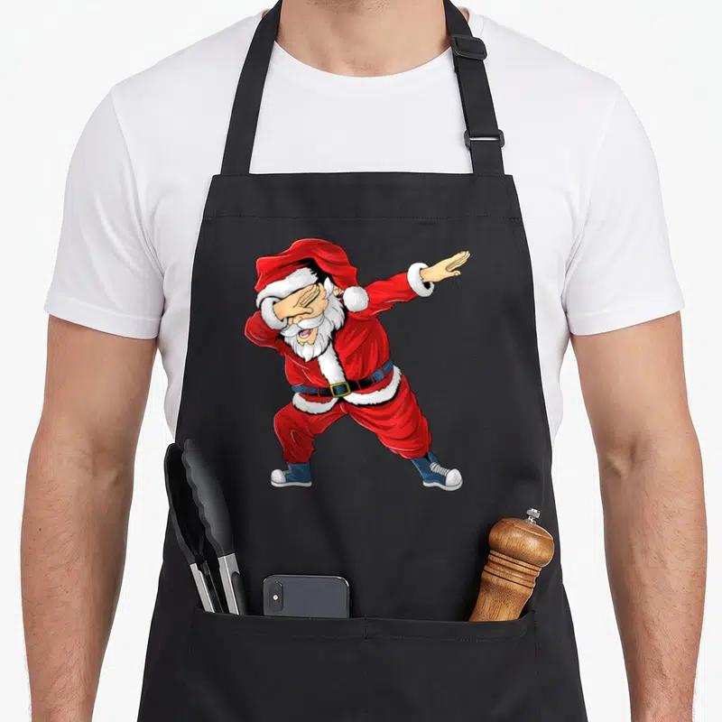 Tablier de cuisine noir avec un Père Noël rouge effectuant une pose dab moderne et humoristique.