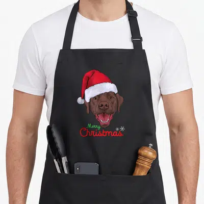 Tablier de cuisine noir avec un Labrador marron portant un bonnet de Père Noël et le texte Merry Christmas en bas.