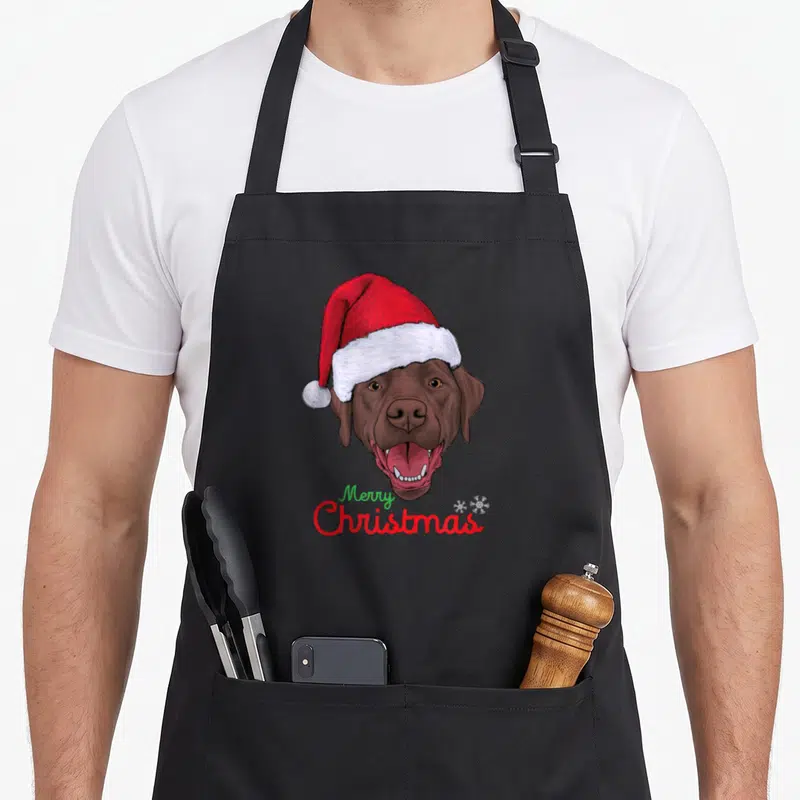 Tablier de cuisine noir avec un Labrador marron portant un bonnet de Père Noël et le texte Merry Christmas en bas.