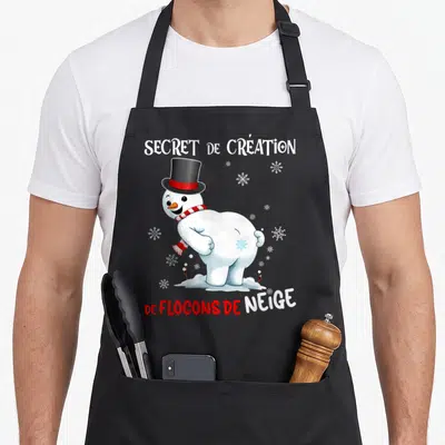 Tablier de cuisine noir avec un bonhomme de neige en chapeau haut de forme et l'inscription Secret de création de flocons de neige.