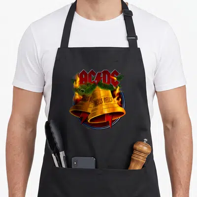 Tablier de cuisine noir avec logo AC/DC rouge, deux cloches dorées Hells Bells, feu et branches de sapin vertes.