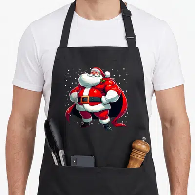 Tablier de cuisine noir avec illustration d'un père Noël super héros musclé portant un bonnet rouge et une cape noire.