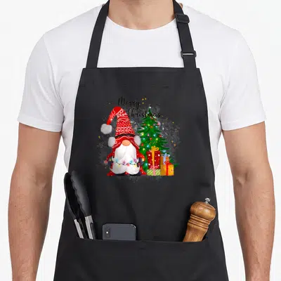 Tablier de cuisine noir avec une gnomie rouge, un sapin illuminé et des paquets cadeaux colorés.