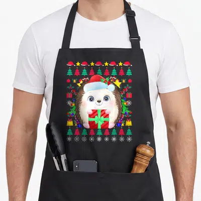 Tablier de cuisine noir avec hérisson drôle portant un bonnet de père Noël et tenant un cadeau rouge à ruban vert.