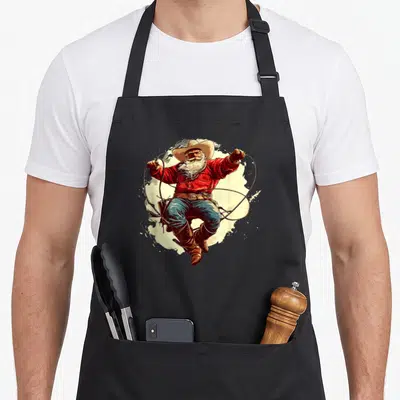 Tablier de cuisine noir avec un Père Noël cowboy en chapeau, chemise rouge et lasso en mouvement.