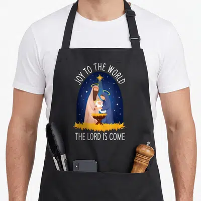 Tablier de cuisine noir avec illustration d'une crèche de Noël et textes en anglais.